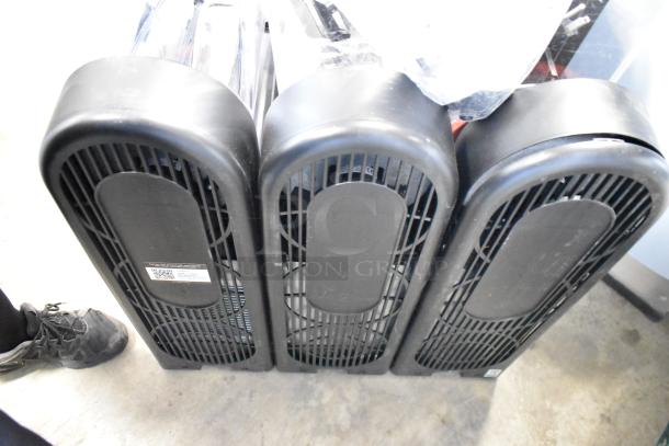 Three black tower fans, in used condition, with front grilles; one fan has a visible label with a QR code and product details.