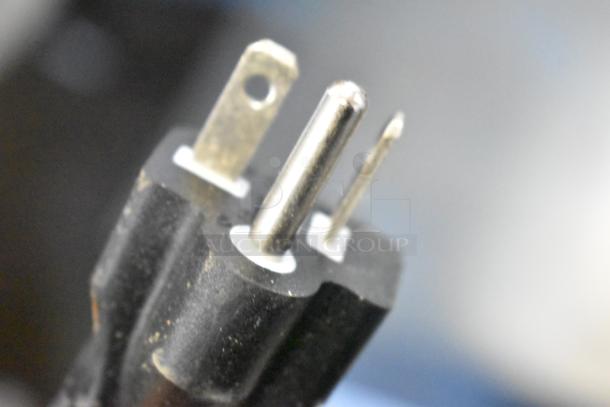 Close-up of a black, three-prong electrical plug with slight wear, suitable for high-voltage devices.
