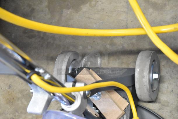 Industrial floor cleaning machine with yellow cord, gray wheels, and metal components, in good condition.
