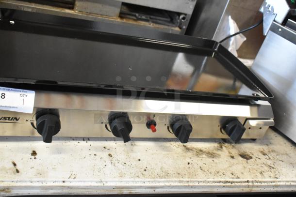 Stainless steel four-burner griddle with control knobs, lightly used, small surface scratches. Auction tag visible, indicating item number.