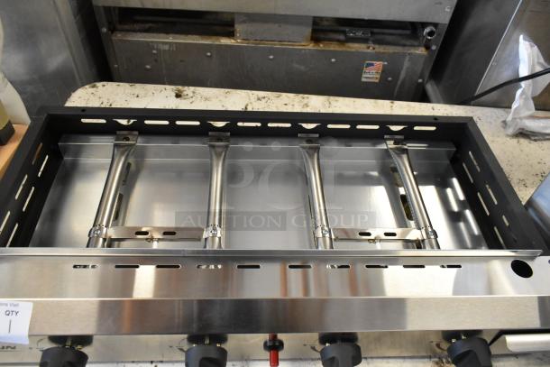 Stainless steel commercial gas grill with four burners, metal frame, and control knobs. Excellent condition.