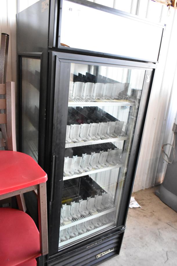 Glass-front vending machine with three shelves, black exterior, labeled "True" at the bottom, in used condition.