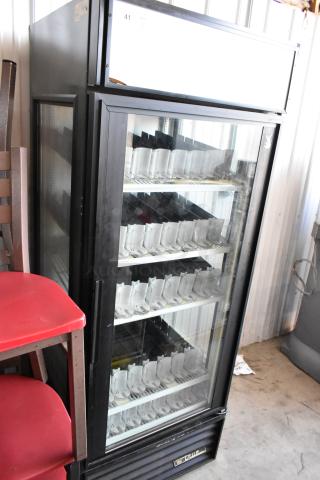 Glass-front vending machine with three shelves, black exterior, labeled "True" at the bottom, in used condition.