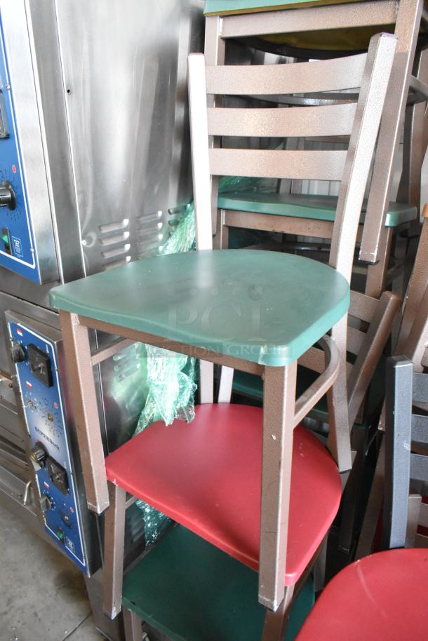 Stacked metal chairs with green and red seats, featuring ladder-back design. Some wear visible, suitable for indoor use.