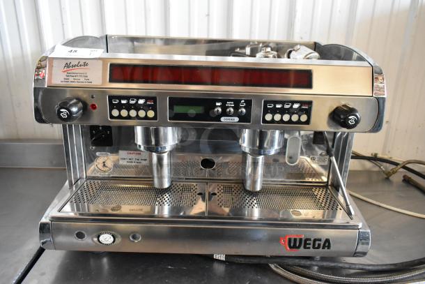 Wega espresso machine with dual group heads, stainless steel finish, programmable buttons, visible wear, branded logo.