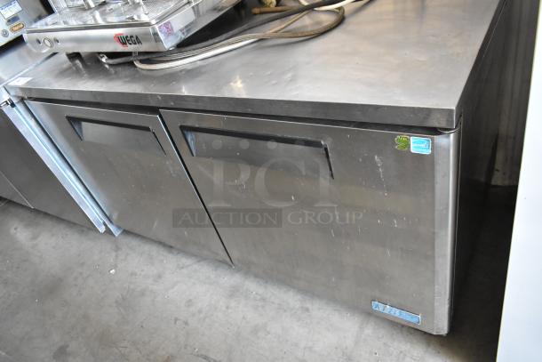 Commercial stainless steel two-door undercounter fridge with visible wear. Features energy certification labels.