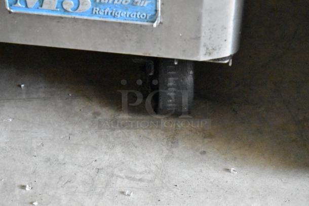 Turbo Air refrigerator caster wheel and corner, showing moderate wear, with visible manufacturer's logo and text.