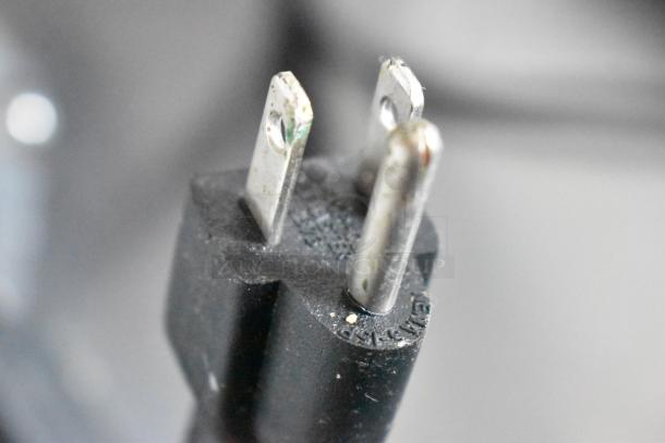 Close-up of a three-prong electrical plug with a black casing. Slight discoloration on metal prongs. Textured surface with molded markings.