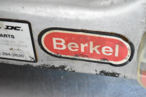Close-up of a worn Berkel machine label on metal. Red logo with white letters. Visible wear indicates age.
