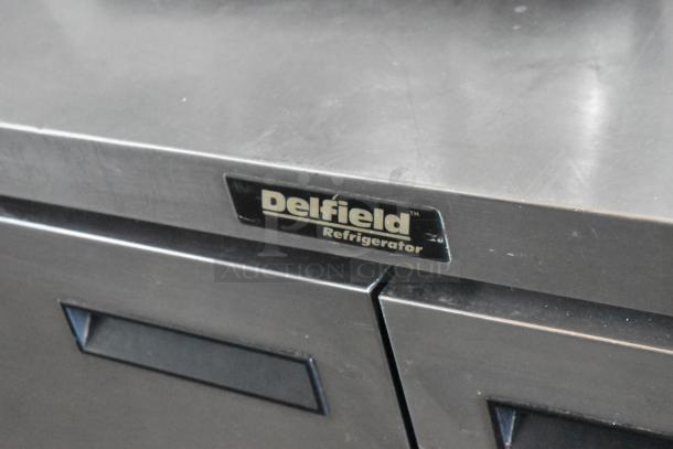 Delfield refrigerator with stainless steel exterior, showing minimal wear. Brand label visible on door handle.