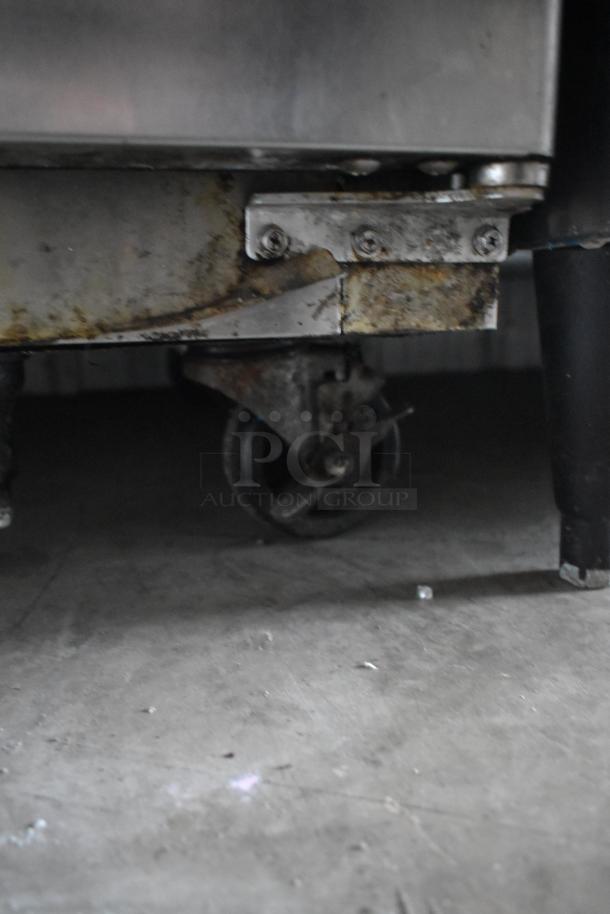 Close-up of a metal object with a rusty caster wheel on a concrete floor. Some surface rust and wear visible.