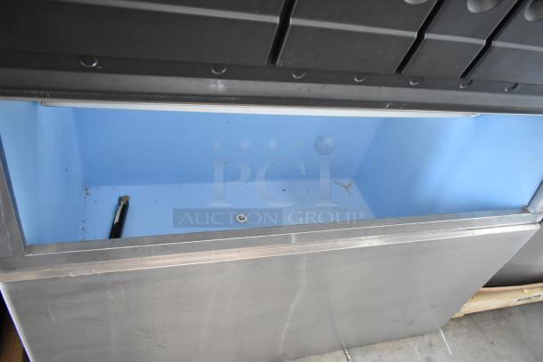 Commercial stainless steel ice bin with blue interior, in used condition, visible drainage hole, and black ice scoop included.
