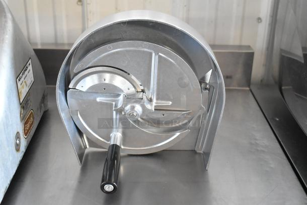 Commercial tomato slicer with hand-crank, stainless steel, excellent condition, visible brand Kelajbrass inc., mounted on metal surface.