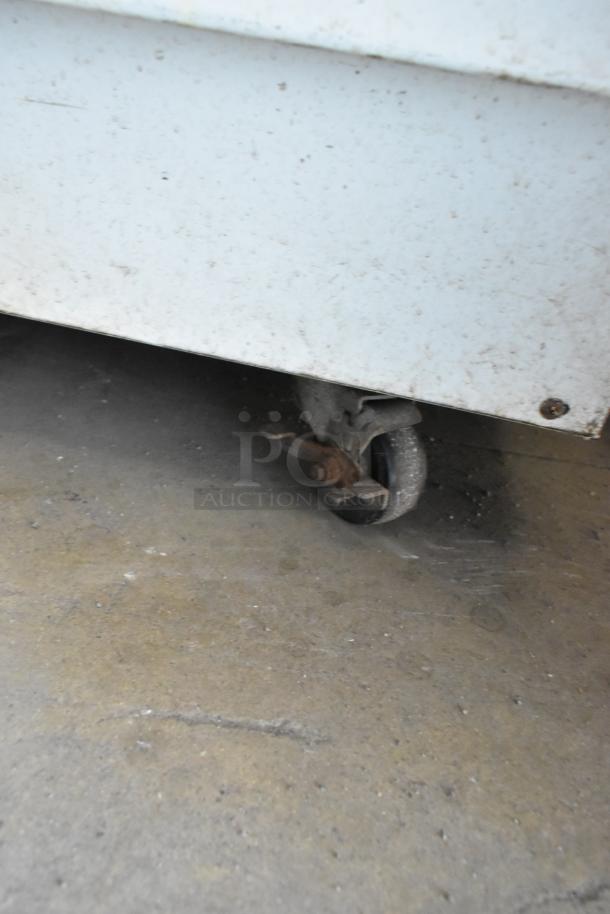 Metal caster wheel on a white industrial cart, showing rust and signs of wear. Suitable for heavy-duty applications.