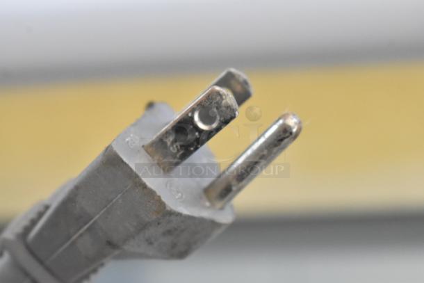 Close-up of a worn metallic two-prong electrical plug. Markings visible on prongs suggest identification or usage information.