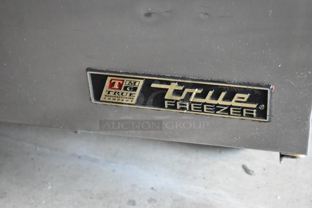 True freezer logo on metal surface, from True Manufacturing Company. Slight scratches visible, indicating used condition.