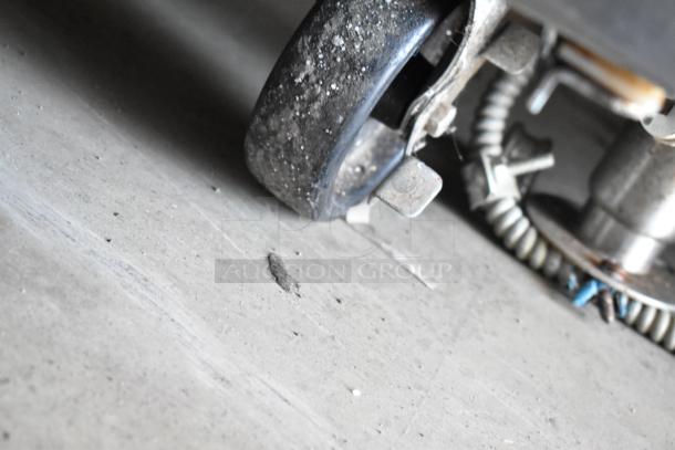 Close-up of a dusty, swivel caster wheel and adjacent metal components on concrete, part of a larger industrial machine.