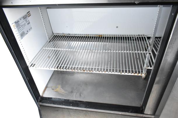 Commercial refrigerator interior with wire shelves. Shows wear and rust. True model label indicates specifications.