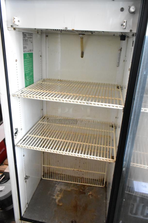 Commercial glass-door refrigerator, three wire shelves, signs of rust and wear. Interior label showing specs and instructions.