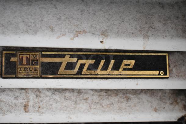 Close-up of a weathered True Manufacturing label from St. Louis with gold lettering on a dark background.