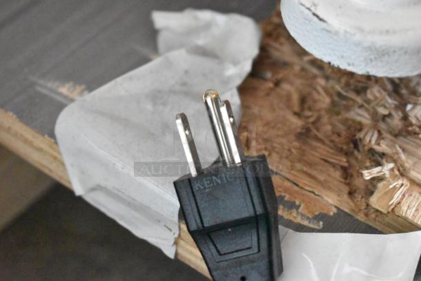 Black electrical plug with "KENIC" imprint, metal prongs visible, resting on a damaged wooden surface.