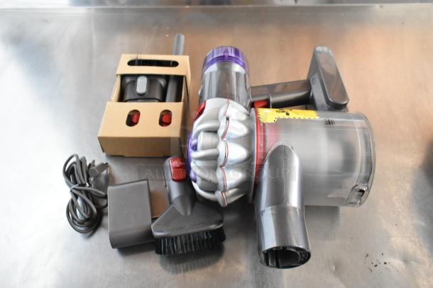 Handheld vacuum cleaner with attachments and charger, featuring a transparent dust canister and purple accents, in used condition.