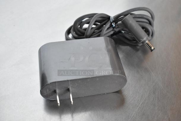 Black power adapter with attached cord, two prongs, slightly scuffed surface.