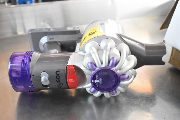 Dyson handheld vacuum, gray and purple, filter wash label visible, in good condition, ergonomic design, compact size.
