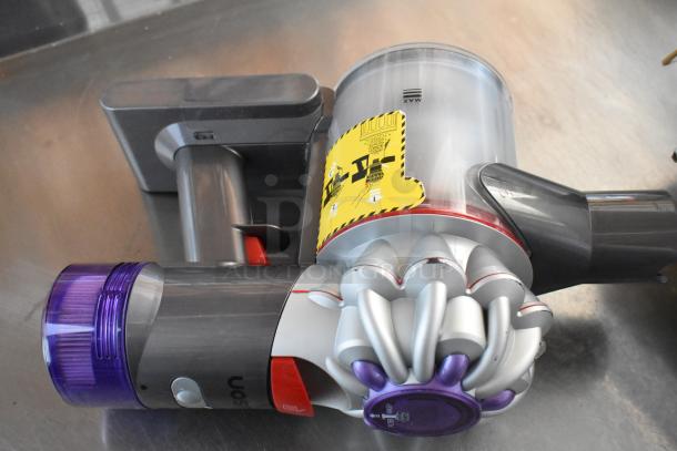 Handheld cordless vacuum cleaner with purple accents. Includes dust container and instructions label. Good condition.