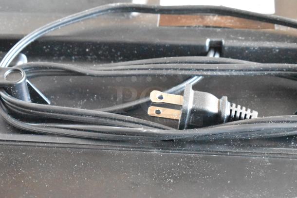 Black two-prong electric power cord, coiled and slightly dusty, in used condition.