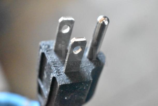 Close-up of a three-prong electrical plug; features two flat blades and one round pin, set in a black plastic housing.
