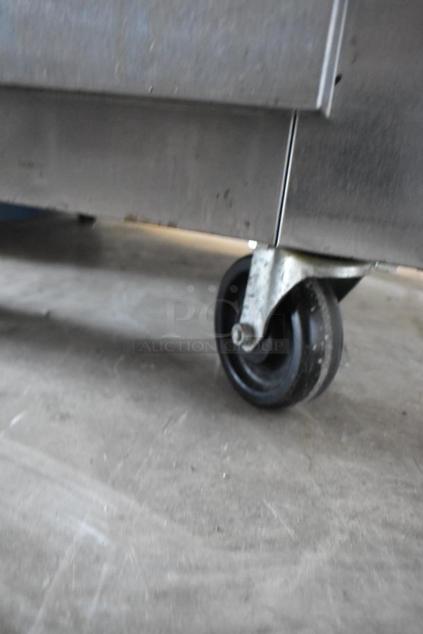 Close-up of a metal equipment caster wheel on a concrete floor, showing some wear and marks. No visible labels.