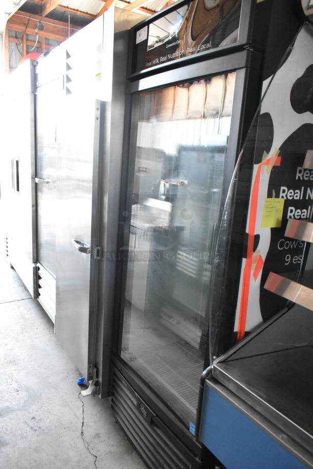 Glass-door commercial refrigerator, black trim, visible interior shelves, and exterior dairy branding sticker, in good condition.