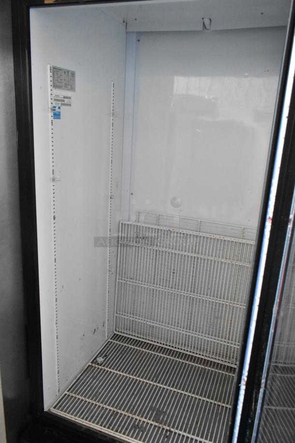 Commercial upright refrigerator, white interior, metal shelves. Visible manufacturer label with specifications. Used condition.