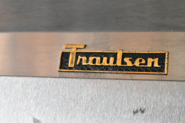 Traulsen stainless steel appliance badge, black and gold logo, slight surface wear visible.