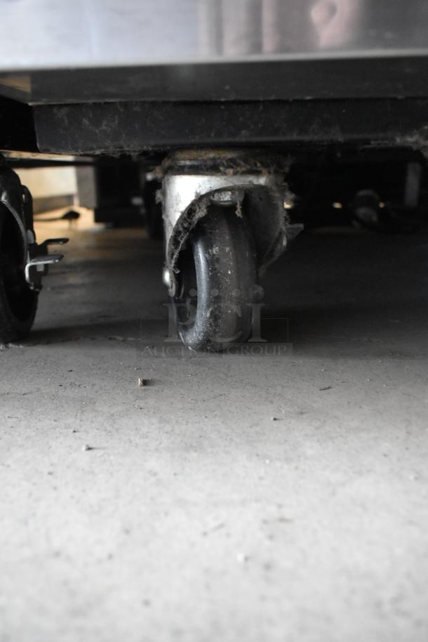 Underside view of a metal caster wheel attached to a heavy-duty object, showing signs of dust and wear.