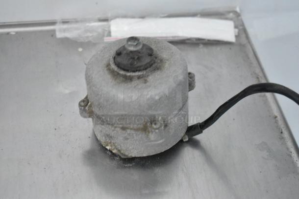 Weathered electric motor with visible wear and cable, placed on a metal surface. No visible labels or markings.