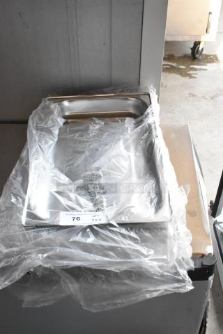 Stainless steel tray, new in plastic wrap, with label indicating lot 76, quantity 6. Suitable for service or display.