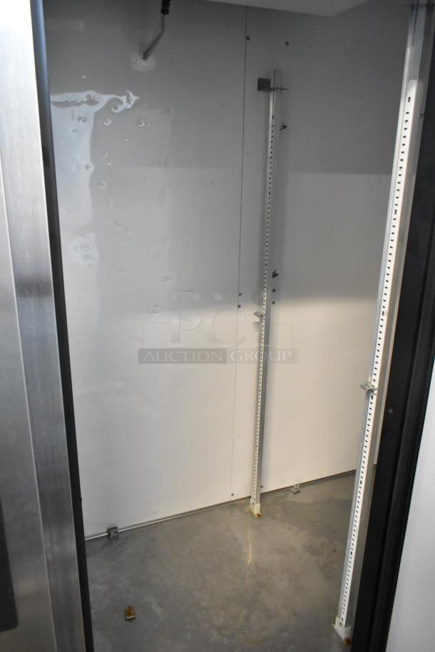 Industrial storage unit interior, empty with white walls, metal shelving supports, and concrete floor. Clean and well-maintained.