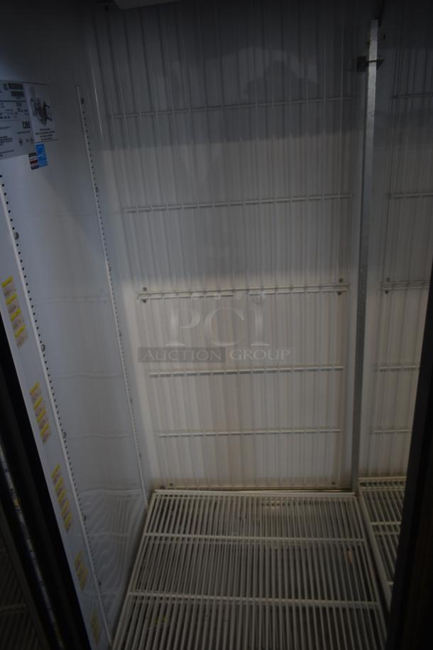 Commercial refrigerator interior, wire shelves, and white back panel. Manufacturer label indicating model and specifications.