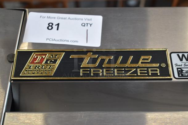 True Freezer with gold-accented logo and auction tag, item 81, on stainless steel surface.