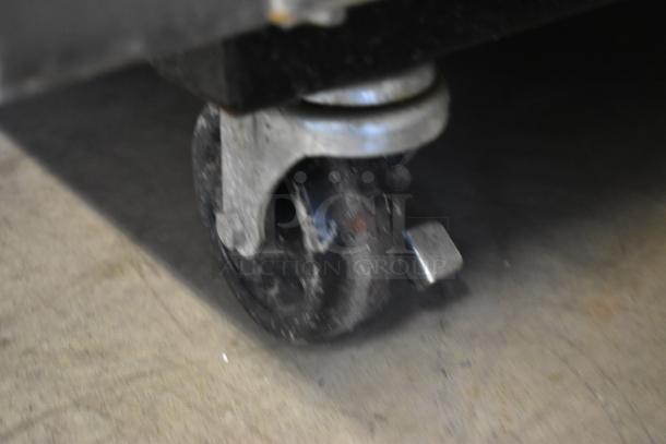 Close-up of a metal caster wheel with a locking mechanism, showing signs of wear, on concrete floor.
