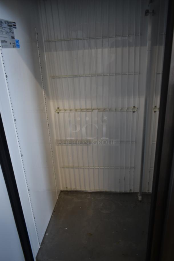 Commercial refrigeration unit interior, white shelves, metal frame. Label indicates brand and model with specifications.