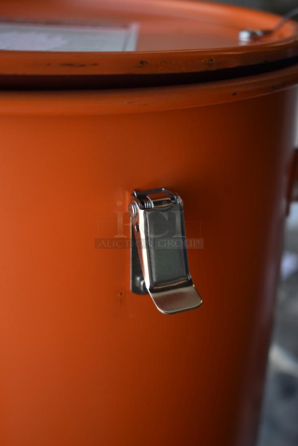 Orange storage drum with metal latch. Slight wear on edges. Lid visible. Suitable for secure storage.