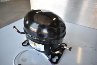 Black compressor unit, model EMC3134U, with visible serial number and attached copper pipes in good condition.