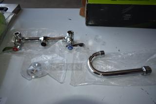Chrome kitchen faucet set, new in packaging. Features dual handles with red and blue indicators. Includes spout and connectors.