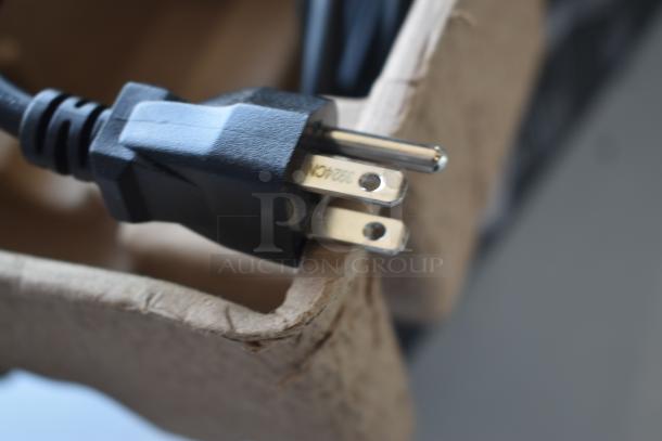 Close-up of a black electrical plug with a metal prong marked "392AON" resting on cardboard packaging. Appears in new condition.