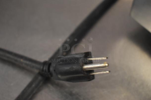 Black three-prong power plug with visible wear on metal prongs, attached to a black cable.