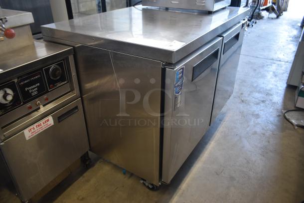 Stainless steel commercial undercounter refrigerator with two doors, on wheels. Label indicates it has a 5-year warranty.