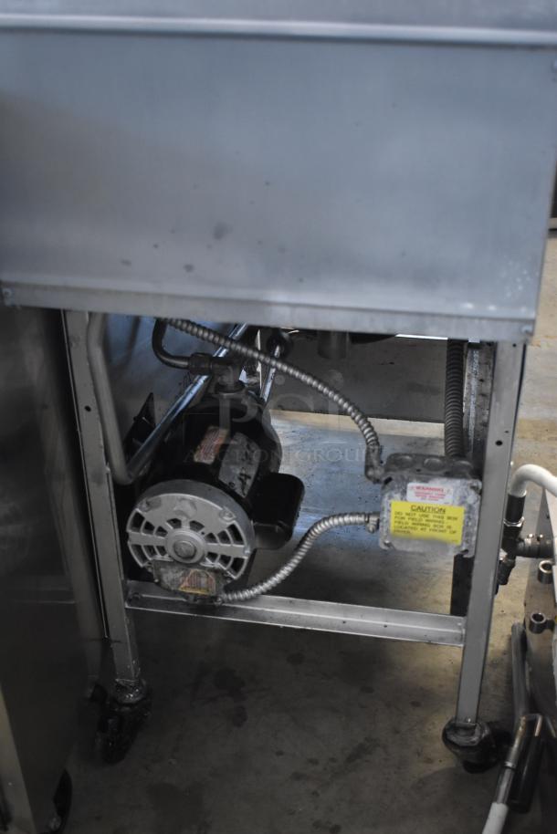 Commercial kitchen sink with visible motor underneath. The motor is partially metal-encased, showing a label with safety warnings. Rust and signs of wear on the metal frame.